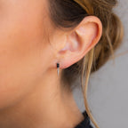 Close-up of a woman's ear wearing the Onyx Dagger Drop Earrings, featuring a small silver design with a baguette-cut onyx and pointed dagger charm.