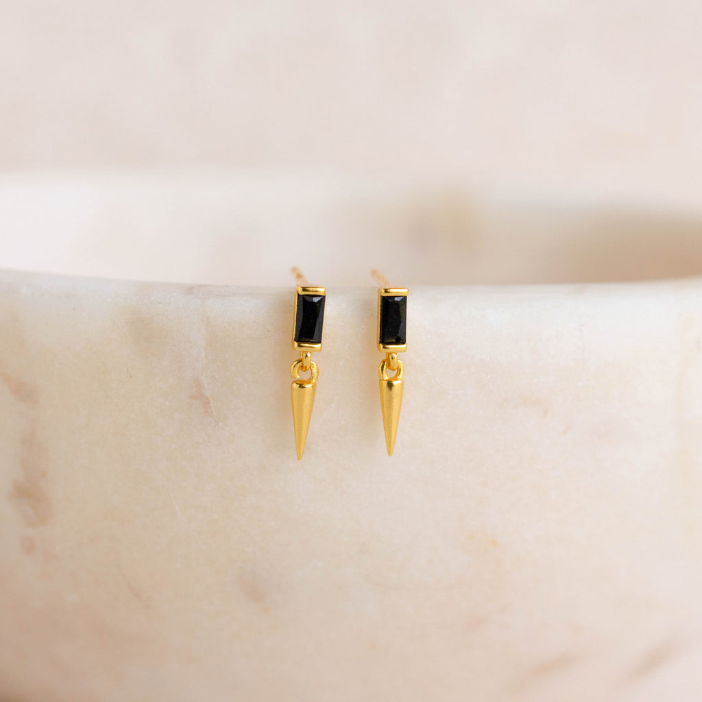 Onyx Dagger Drop Earrings with baguette-cut onyx stones and pointed dagger charms, shown on a light marble surface.