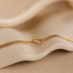 The Love Knot Bracelet features a delicate knot design with double chain detail, elegantly displayed on beige fabric—a perfect gift for couples.