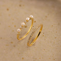 The Pave Pearl Stacking Ring Set features a gold pave pearl ring with small pearls and diamonds, plus a gold ring with a row of small diamonds, shown on a beige surface.