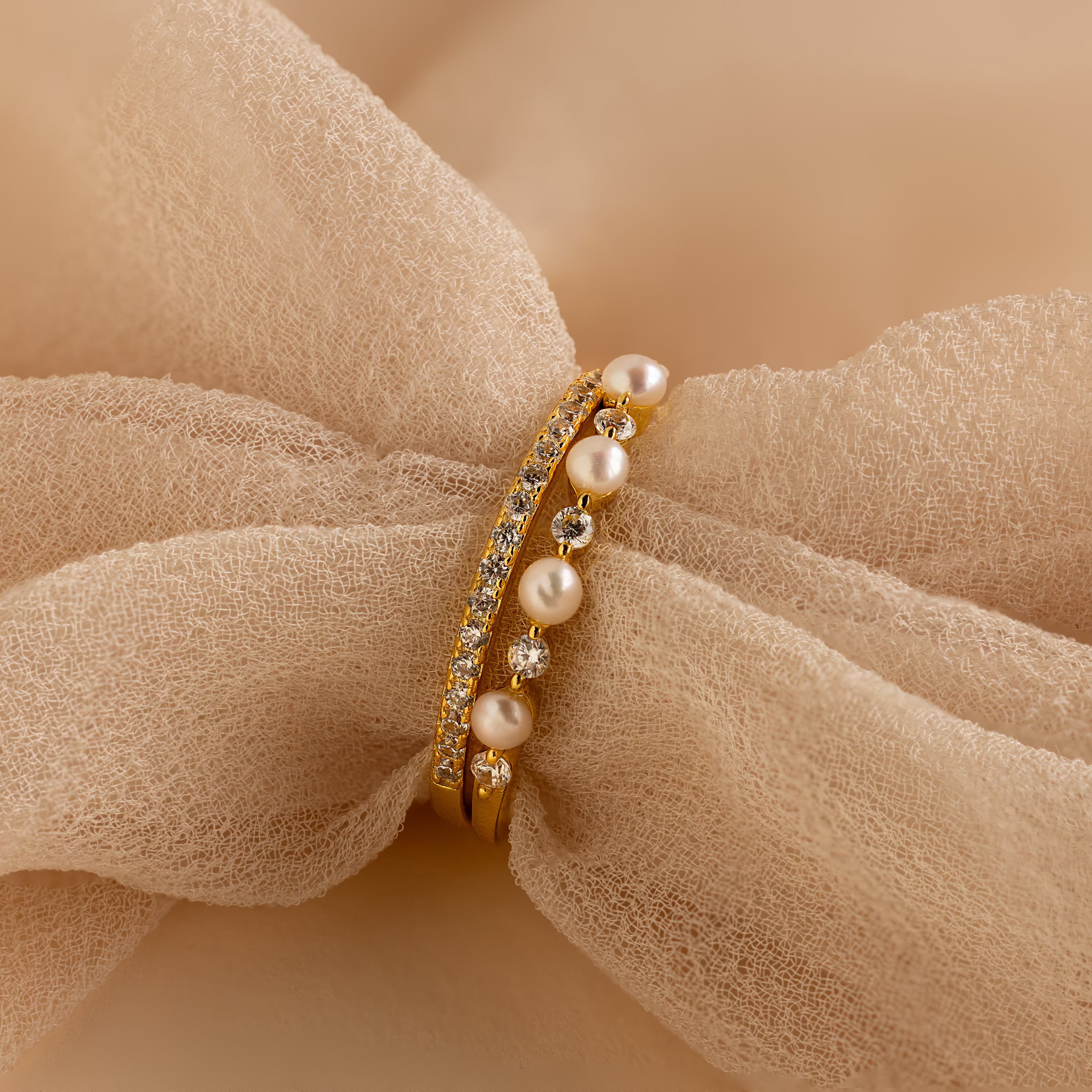 The Pave Pearl Stacking Ring Set, adorned with small diamonds, is displayed on soft beige fabric—an ideal choice for lovers of elegant gemstone rings.