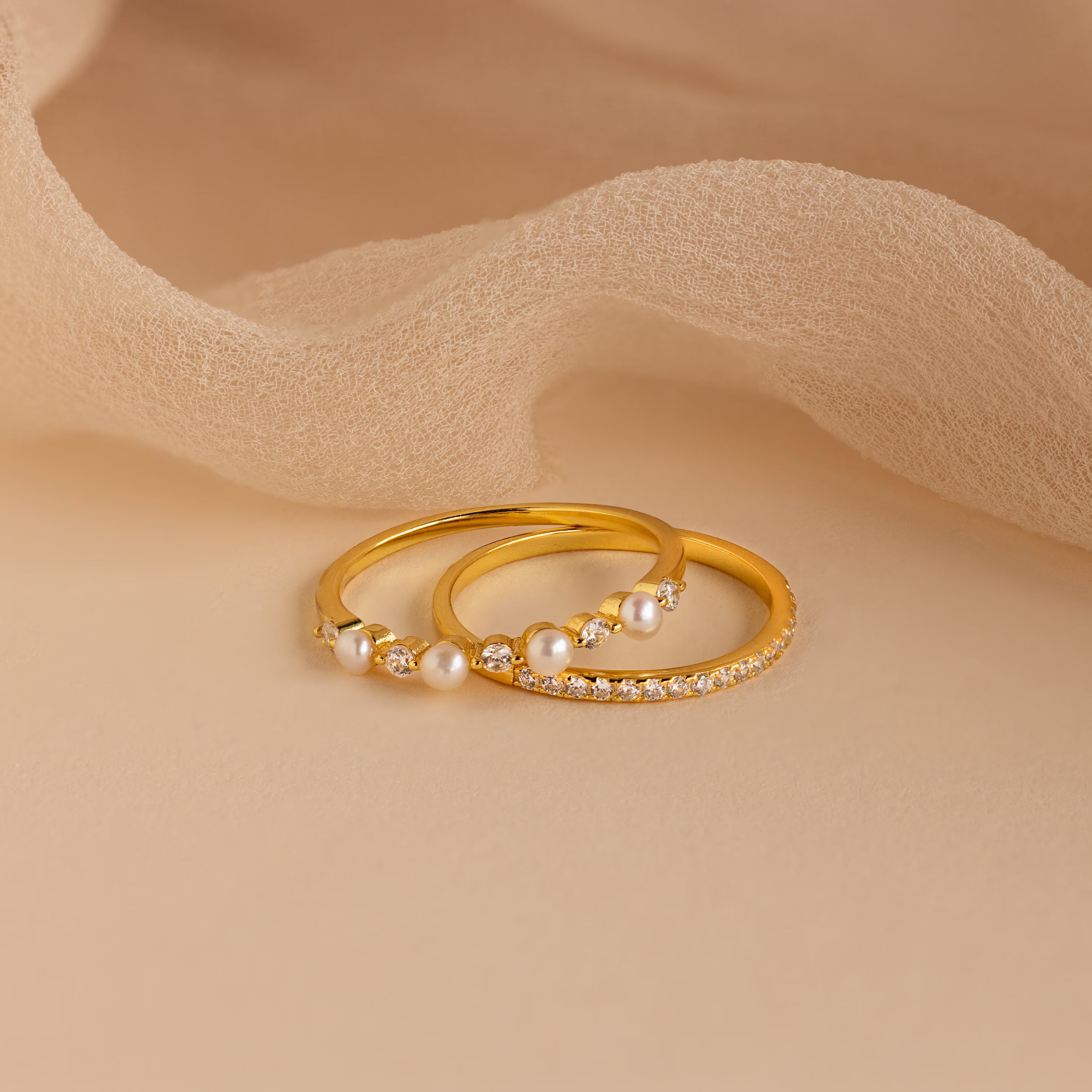The Pave Pearl Stacking Ring Set, featuring elegant gold bands with shimmering small diamonds, is beautifully displayed on a beige fabric background, emphasizing its timeless charm and sophisticated design.