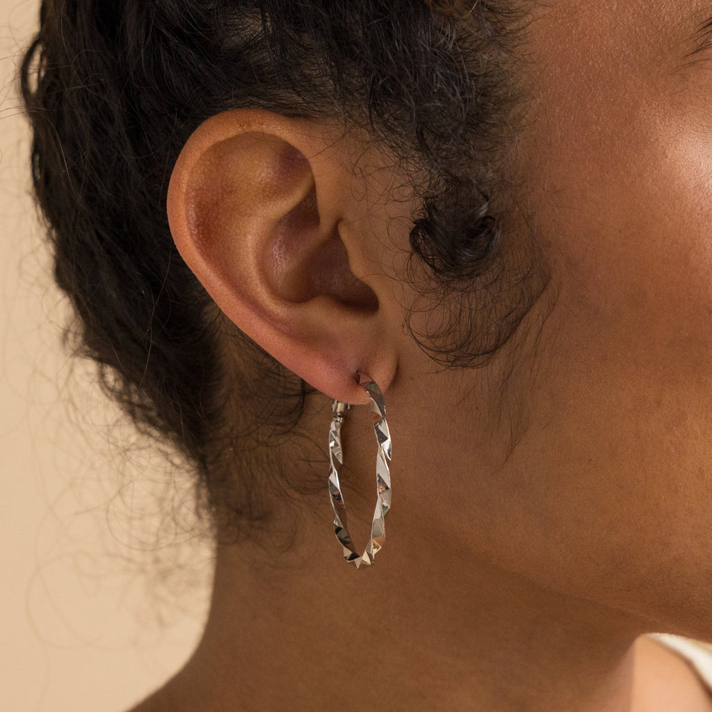 A close-up of a person's ear showcases the Large Twisted Hoops—these statement earrings feature a textured twist design, making them an ideal summer accessory.