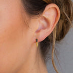 Close-up of a woman's ear wearing Onyx Dagger Drop Earrings, featuring a striking gold dagger charm, with her hair tied back.