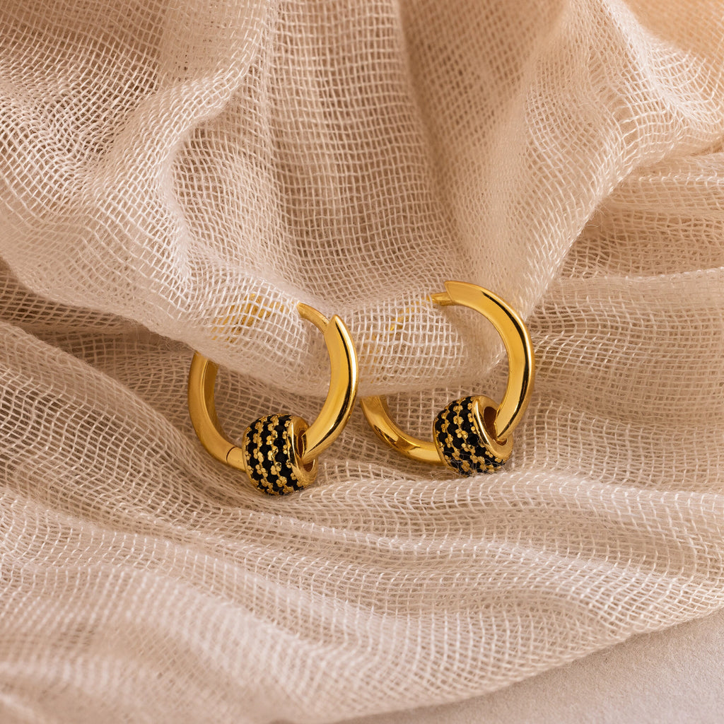 The Onyx Pave Beaded Hoops—gold huggie earrings with black onyx pavé accents—are displayed on lightly textured fabric.