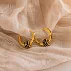 The Onyx Pave Beaded Hoops—gold huggie earrings with black onyx pavé accents—are displayed on lightly textured fabric.
