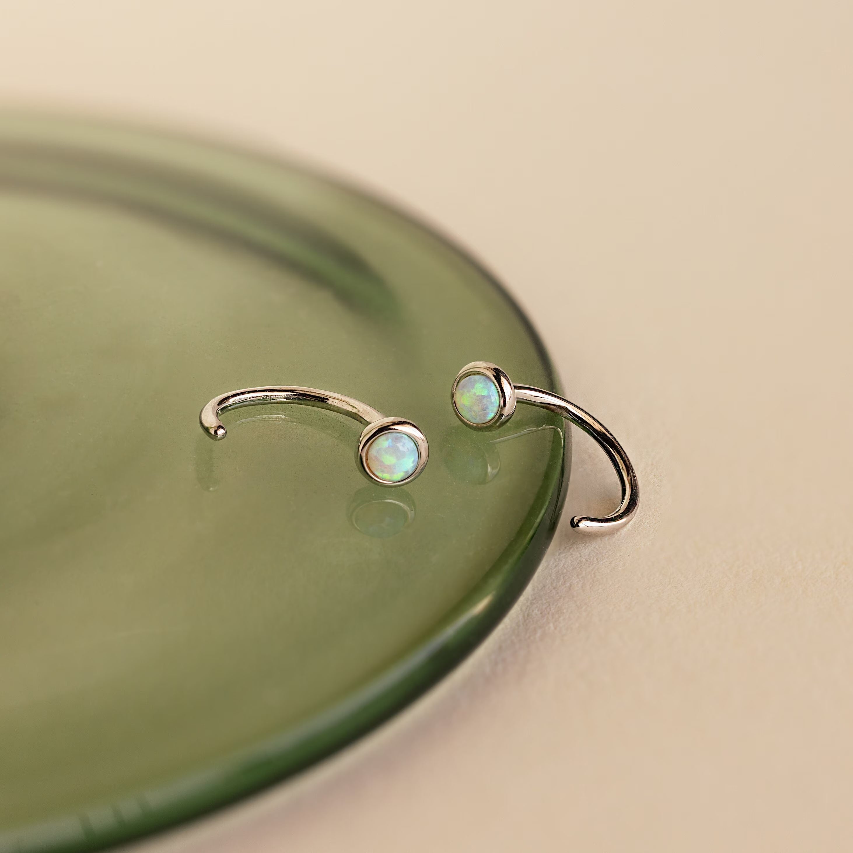 Two Opal Threader Huggies with round stones, shown on a green glass surface—ideal for celestial jewelry lovers.