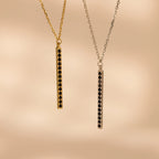 Two Onyx Bar Pendant Necklaces, one gold and one silver, each with a modern vertical row of onyx gemstones in a bar design, displayed on a beige background.