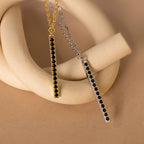 Two Onyx Bar Pendant Necklaces, one in gold and one in silver, each featuring a striking onyx gemstone, are elegantly displayed on a beige sculpture.