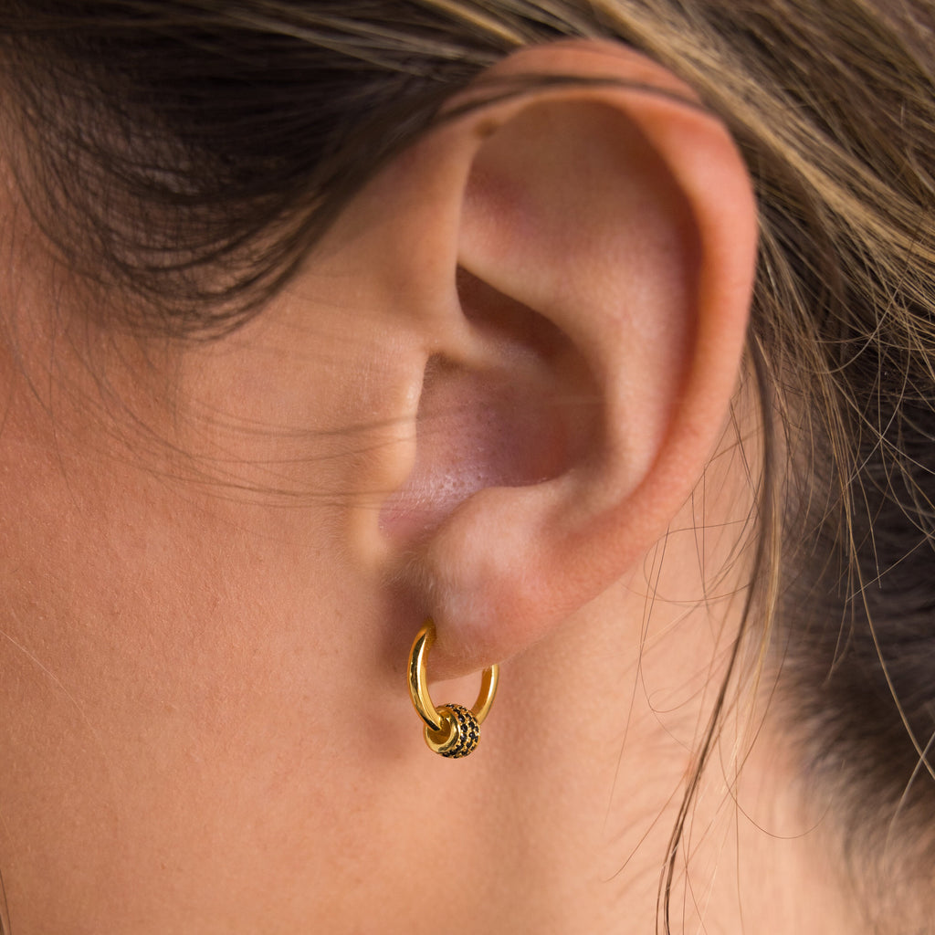 Close-up of a person’s ear wearing the Onyx Pave Beaded Hoops, featuring small gold huggie-style hoops with beaded detailing.