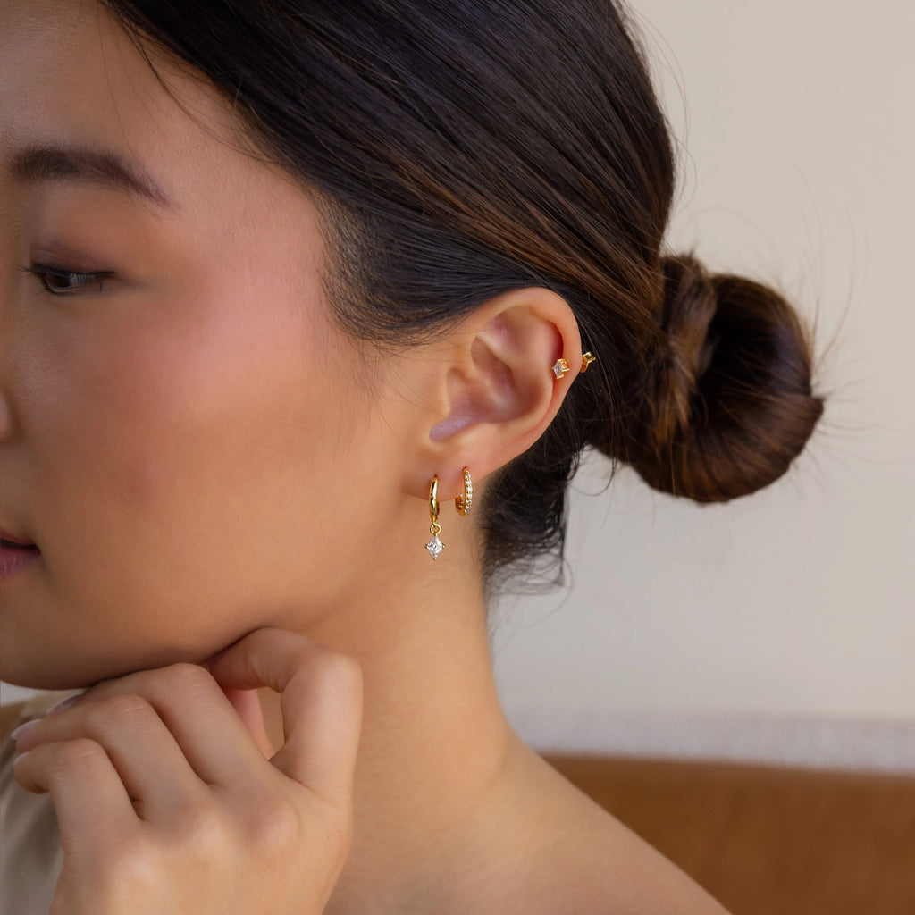 A woman with dark hair in a bun touches her chin, showing her profile and wearing the Diamond Pave Earrings Set.