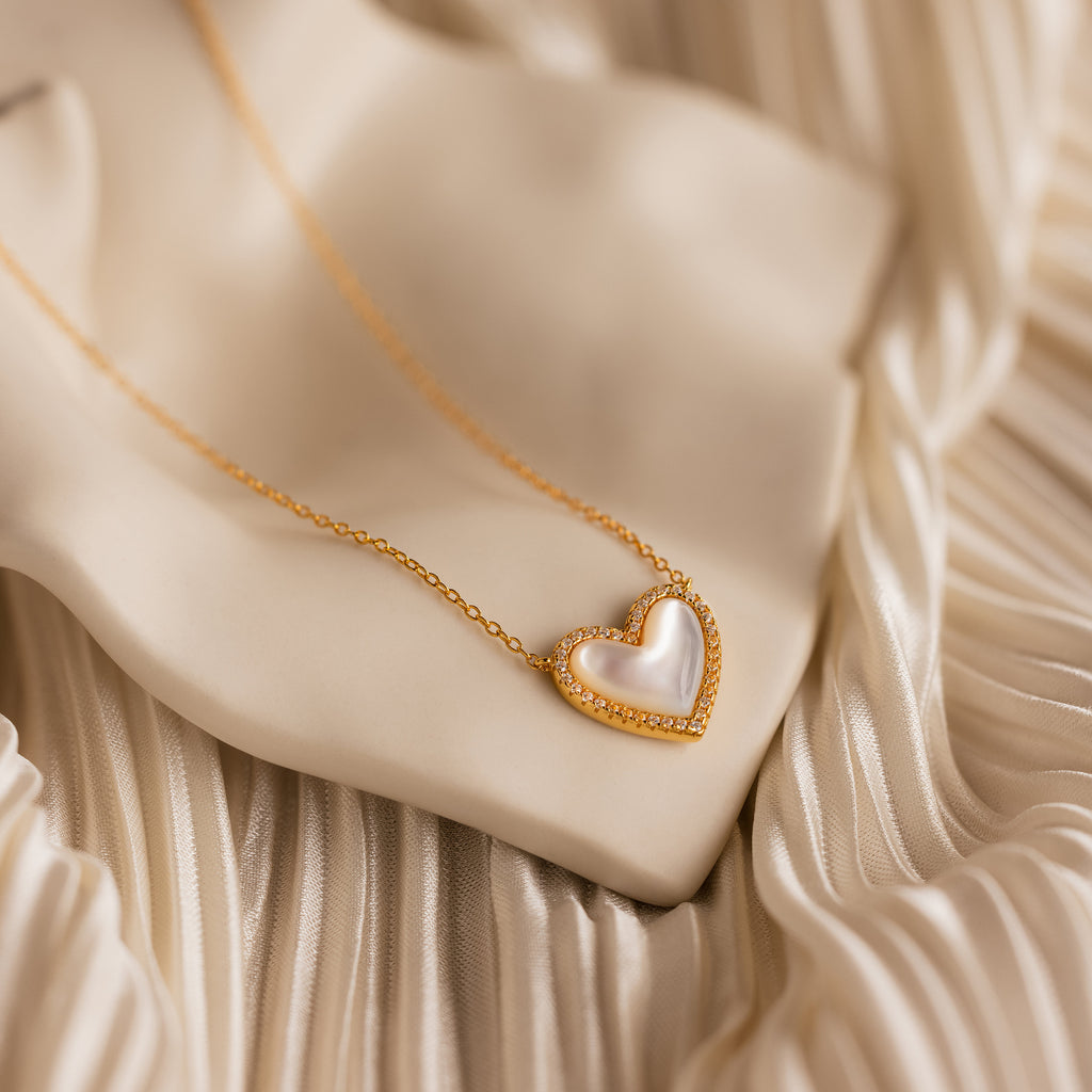 Pave Mother of Pearl Heart Necklace displayed on silky, cream fabric—a timeless, heirloom-inspired jewelry piece with a luminous white heart center, perfect for elevating any collection.