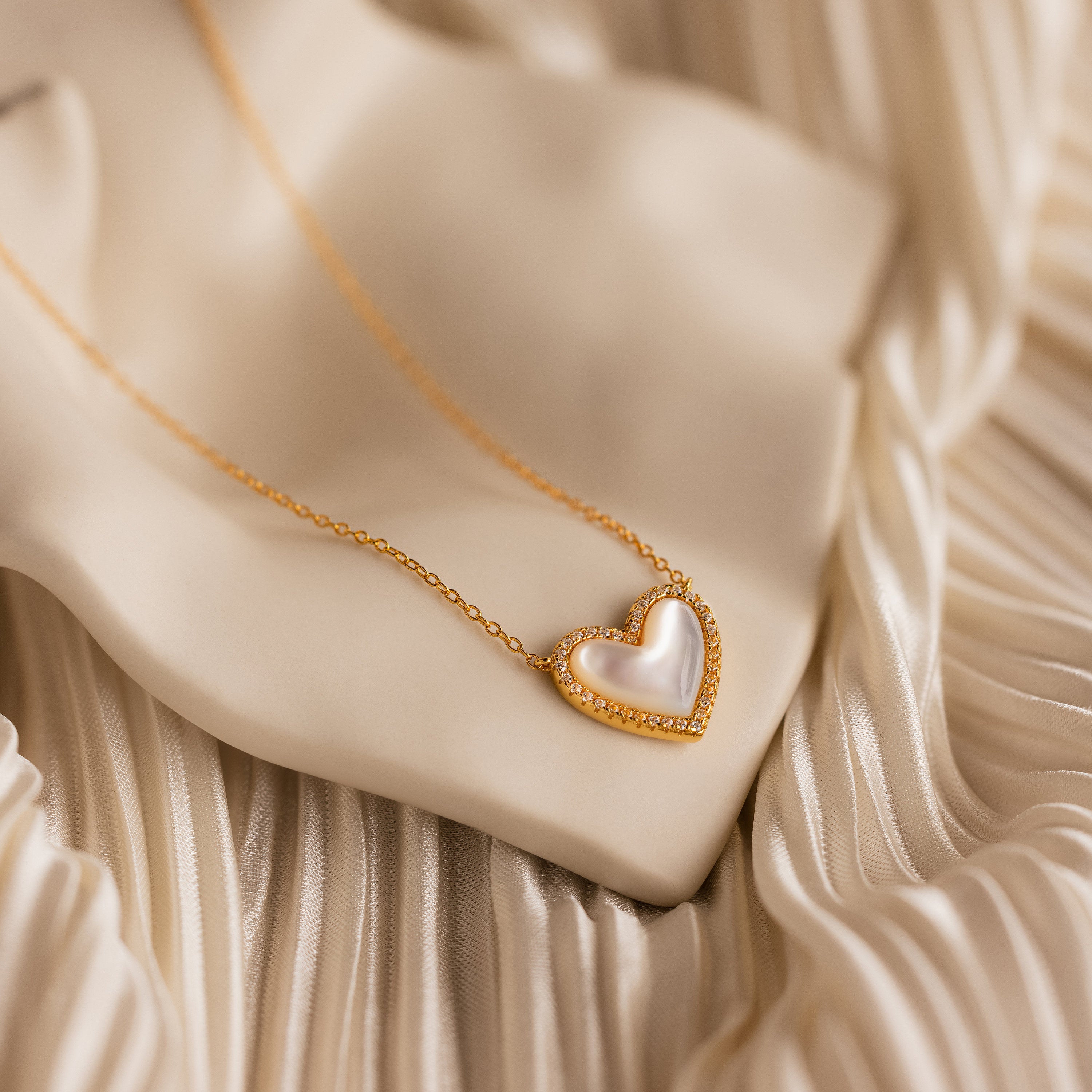 Pave Mother of Pearl Heart Necklace displayed on silky, cream fabric—a timeless, heirloom-inspired jewelry piece with a luminous white heart center, perfect for elevating any collection.