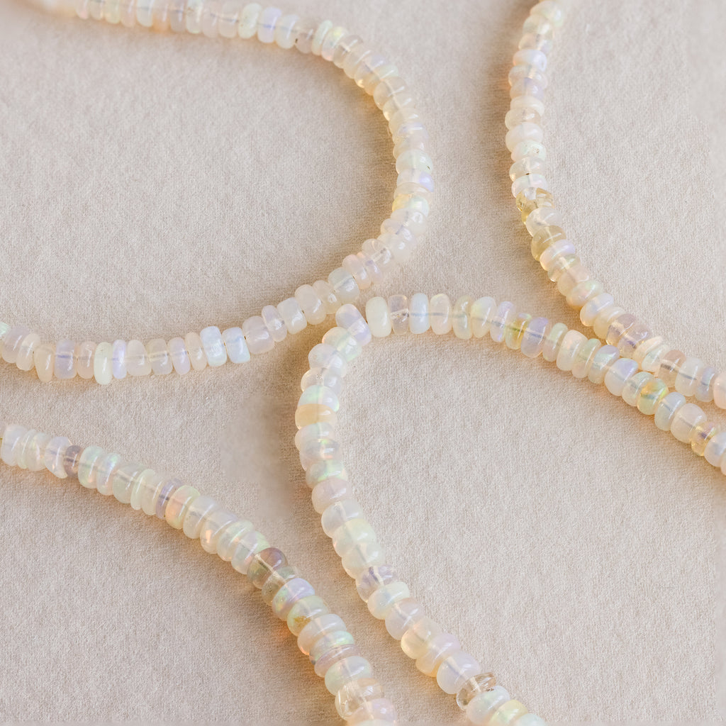 Four strands of round, translucent opal beads curve gracefully on a soft beige background—the Opal Beaded Necklace embodies elegant, bohemian style.