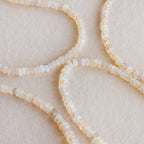 Four strands of round, translucent opal beads curve gracefully on a soft beige background—the Opal Beaded Necklace embodies elegant, bohemian style.