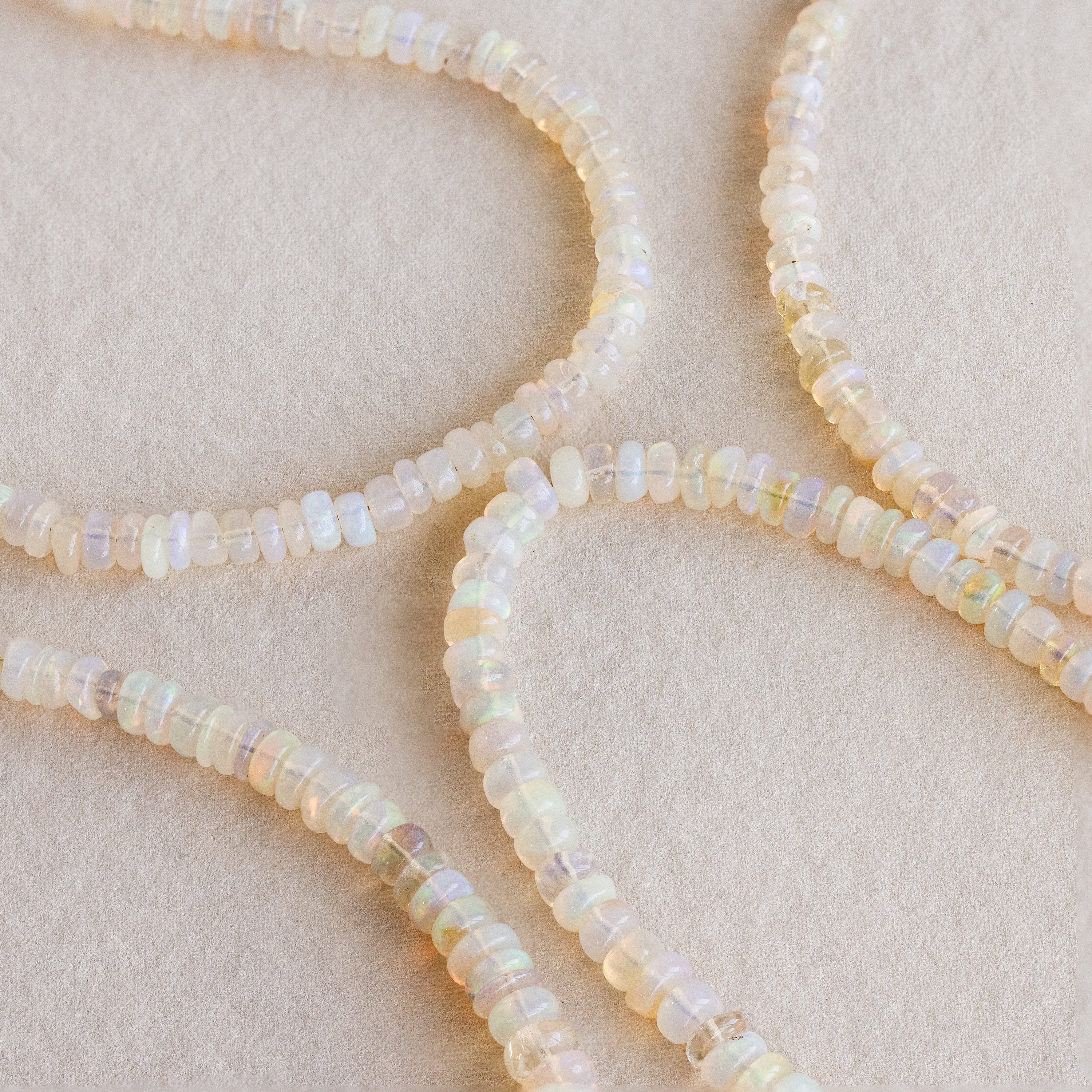 Four strands of round, translucent opal beads curve gracefully on a soft beige background—the Opal Beaded Necklace embodies elegant, bohemian style.