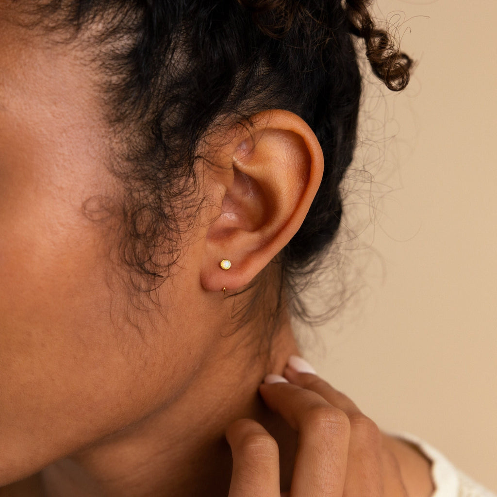A close-up shows a hand touching the neck and curly hair, highlighting Opal Threader Huggies—a refined celestial jewelry piece.