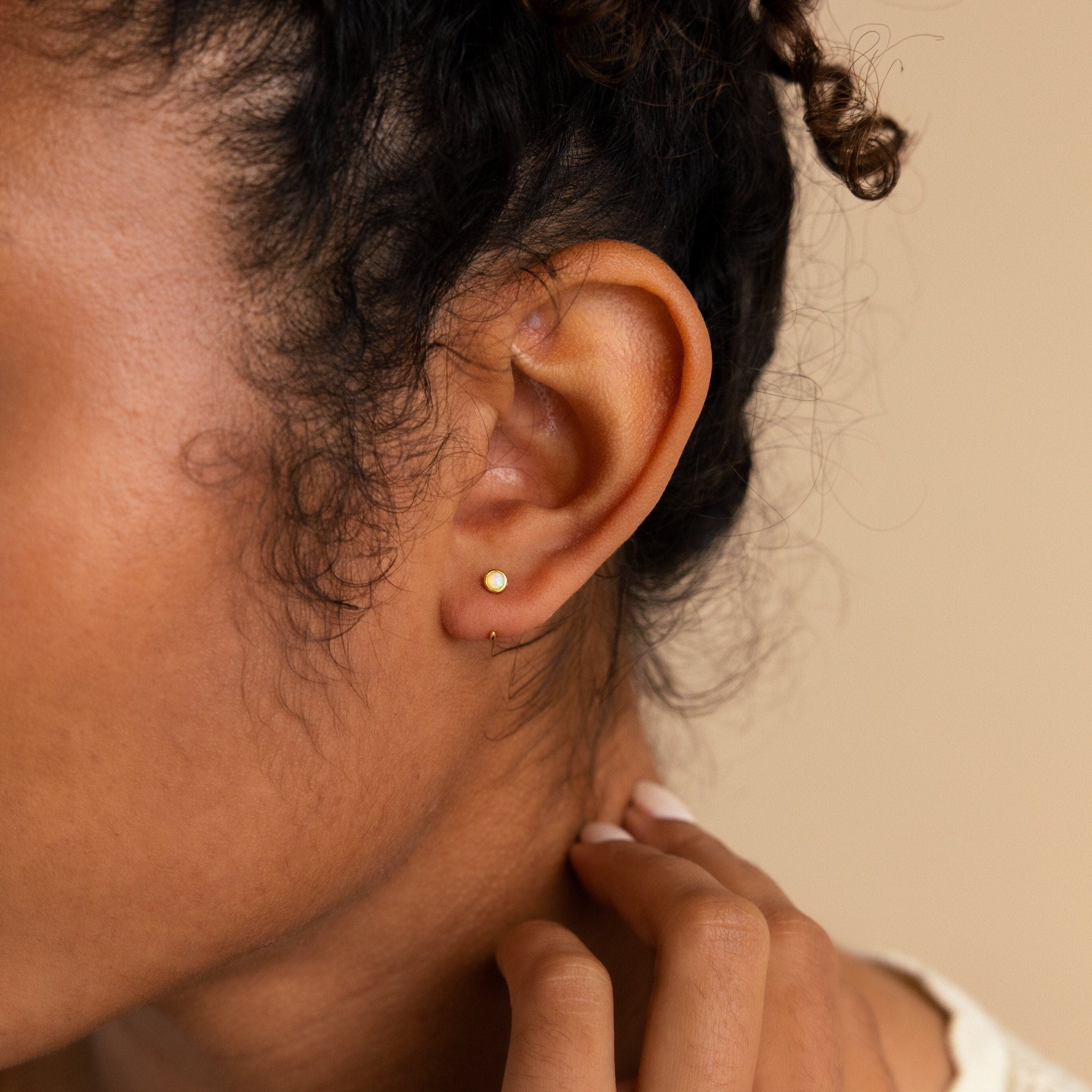 A close-up shows a hand touching the neck and curly hair, highlighting Opal Threader Huggies—a refined celestial jewelry piece.