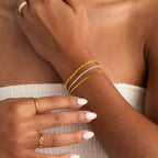 A woman with manicured nails and a white textured strapless top showcases a chic layered look, styled with gold rings and the Curb Chain Bracelet.