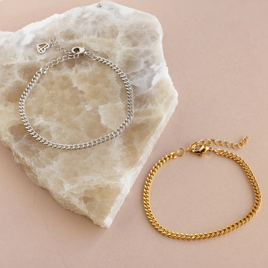 Minimal jewelry shines in the Curb Chain Bracelet, elegantly presented on a light marble slab and beige surface for a chic, layered style.