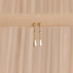 Diamond Pearl Chain Earrings are elegantly displayed on a soft beige fabric background, showcasing their sparkling studs and delicate teardrop pearl charm.