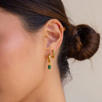 A woman's ear adorned with Emerald Marquise Inlay Huggies and small gold studs, her hair styled in a low bun.