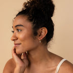 A woman with her hand on her face, showcasing Pear Diamond Drop Hoops that add a touch of sophistication to her look.