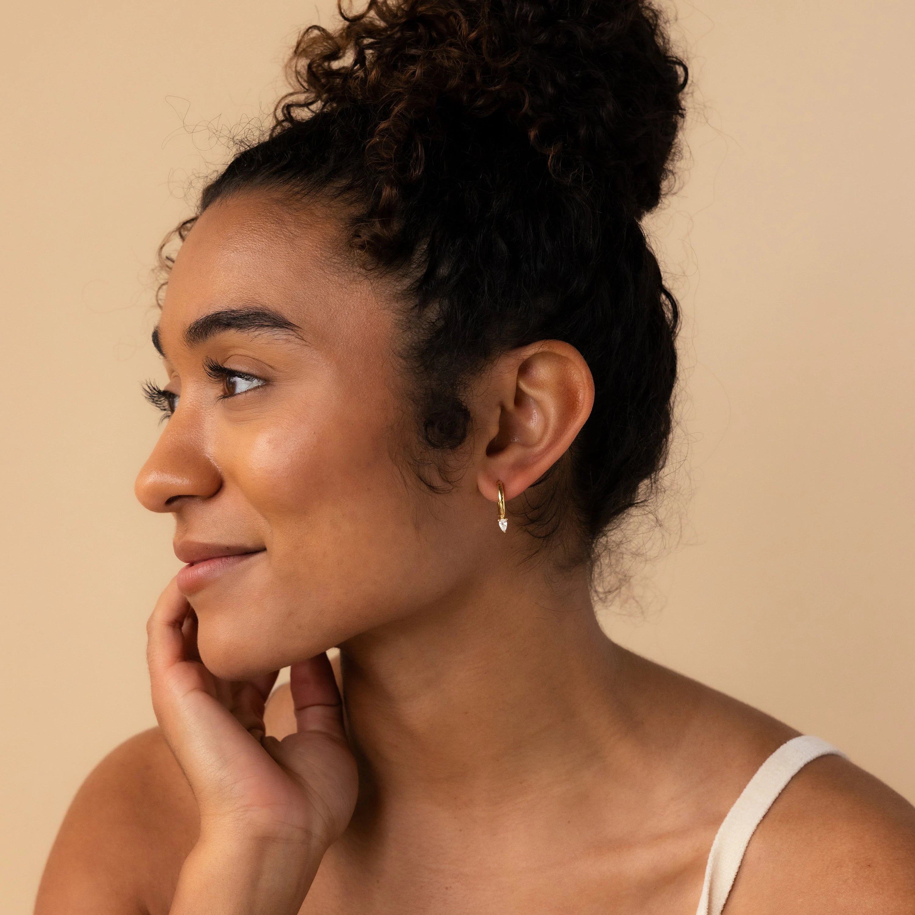 A woman with her hand on her face, showcasing Pear Diamond Drop Hoops that add a touch of sophistication to her look.