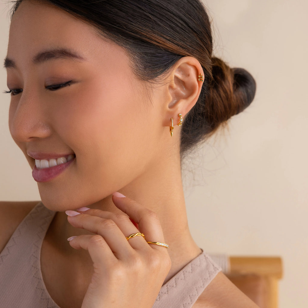 A woman smiles in a beige top and neat low bun, wearing the Ericka Diamond Tennis Huggies—elegant gold earrings accented with diamonds.