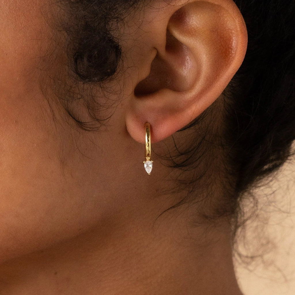 Close-up of an ear wearing Pear Diamond Drop Hoops—small gold hoop earrings with pear-shaped diamond pendants, perfect as a wedding accessory.