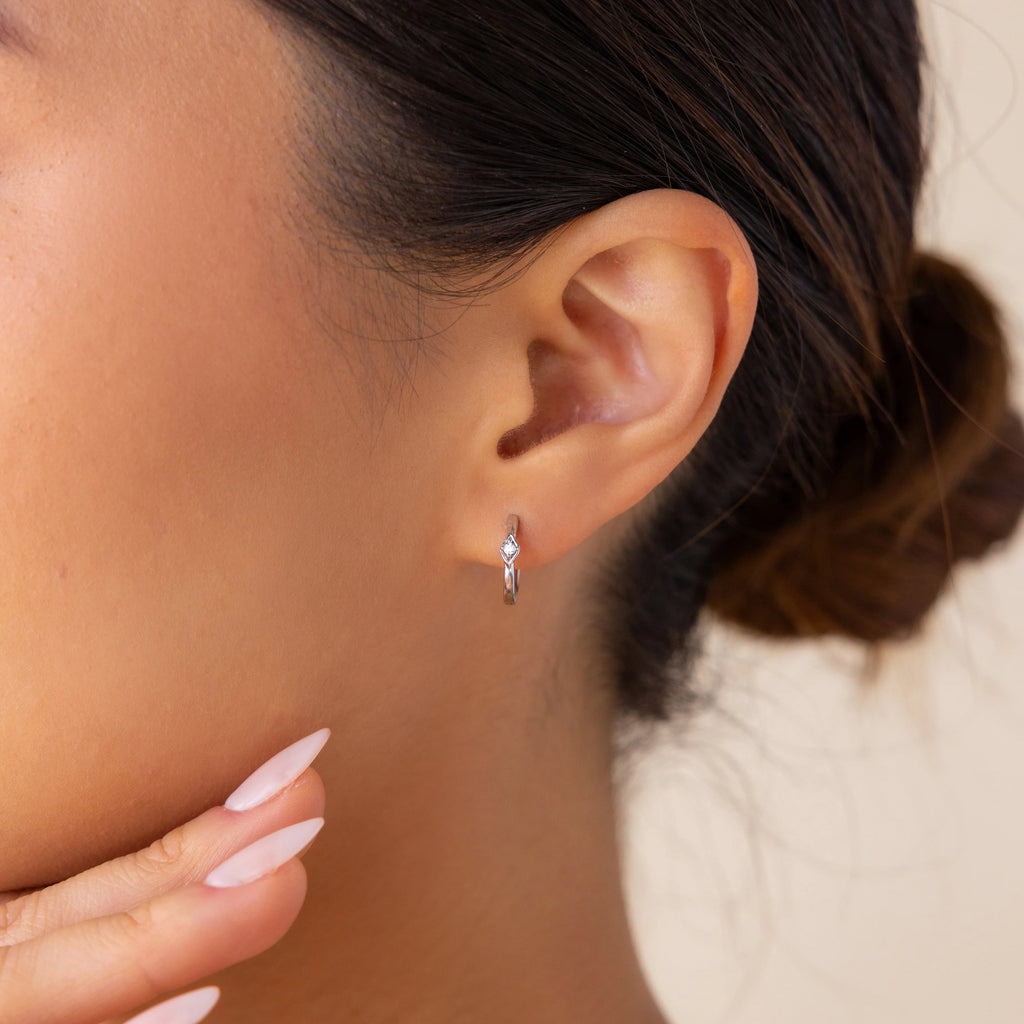 Woman with a neat bun touches her chin, showcasing manicured fingers and wearing minimalist Ericka Diamond Hoops.
