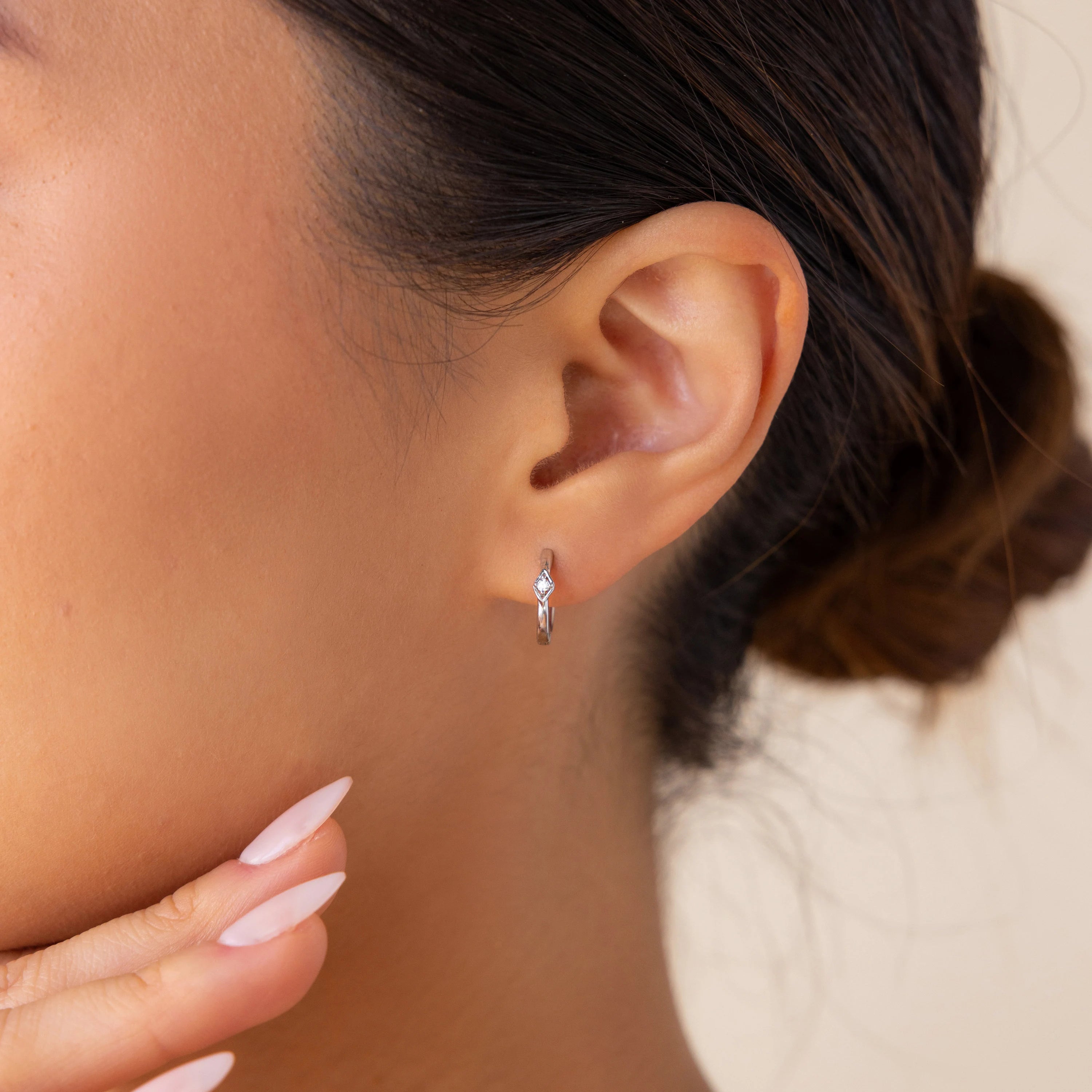 Woman with a neat bun touches her chin, showcasing manicured fingers and wearing minimalist Ericka Diamond Hoops.
