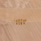 Five pairs of gold Ericka Diamond Hoops and other minimalist huggie earrings, featuring small diamonds, are displayed on a beige textured fabric background.