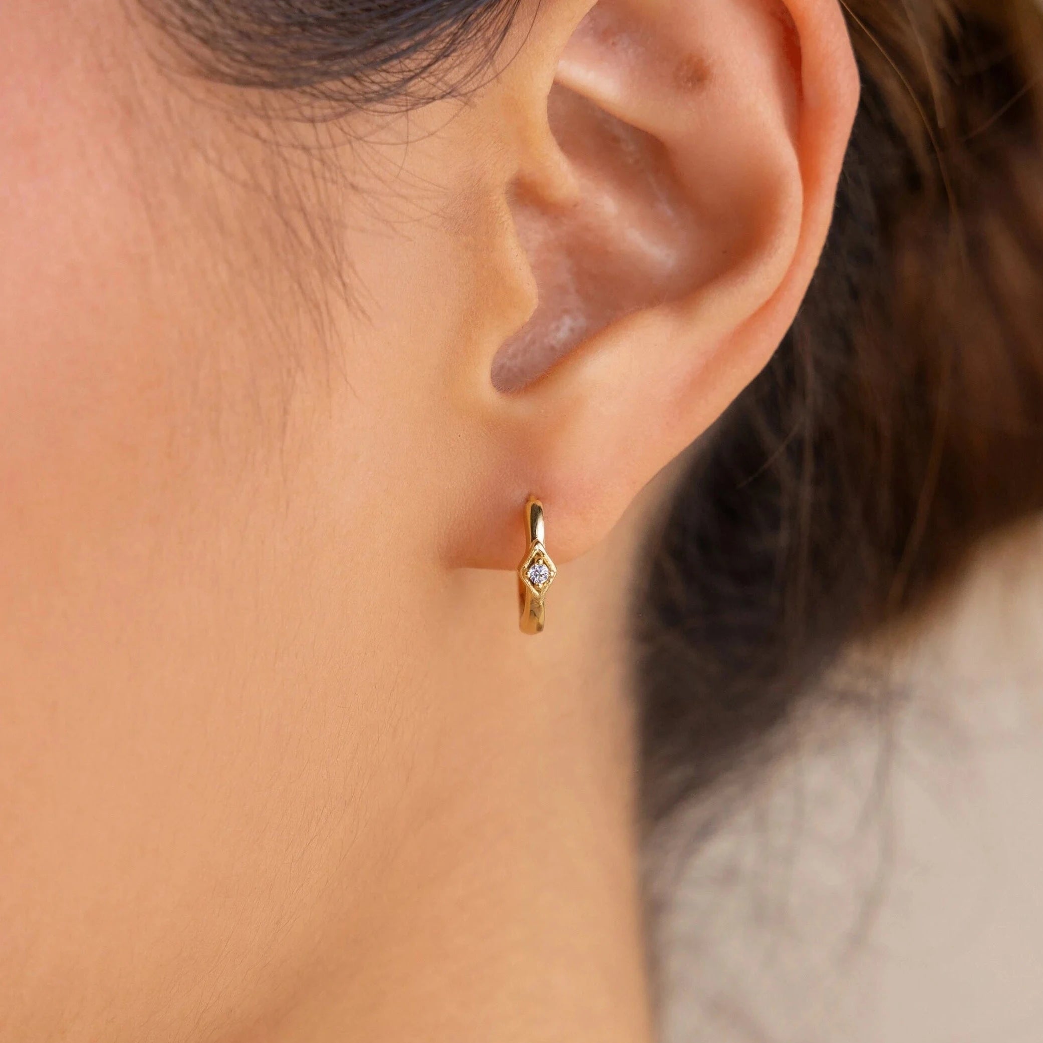 Close-up of an ear wearing the Ericka Diamond Hoops—a minimalist gold huggie earring featuring a tiny diamond accent for subtle sparkle.