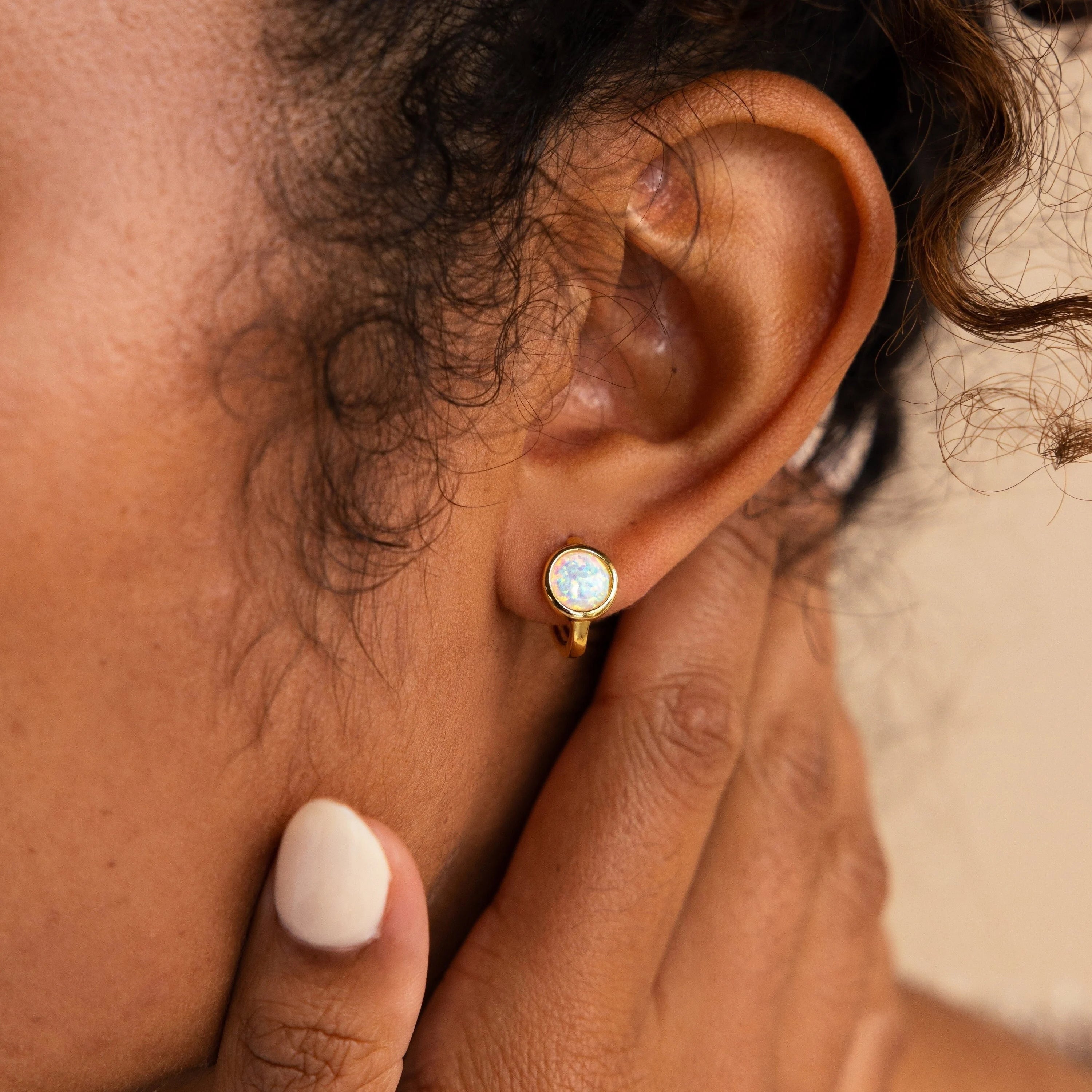 Close-up of a person wearing a round opal stud earring with a gold setting, touching their neck—ideal for pairing with dainty hoops or our Opal Signet Huggies for an added touch of elegance.