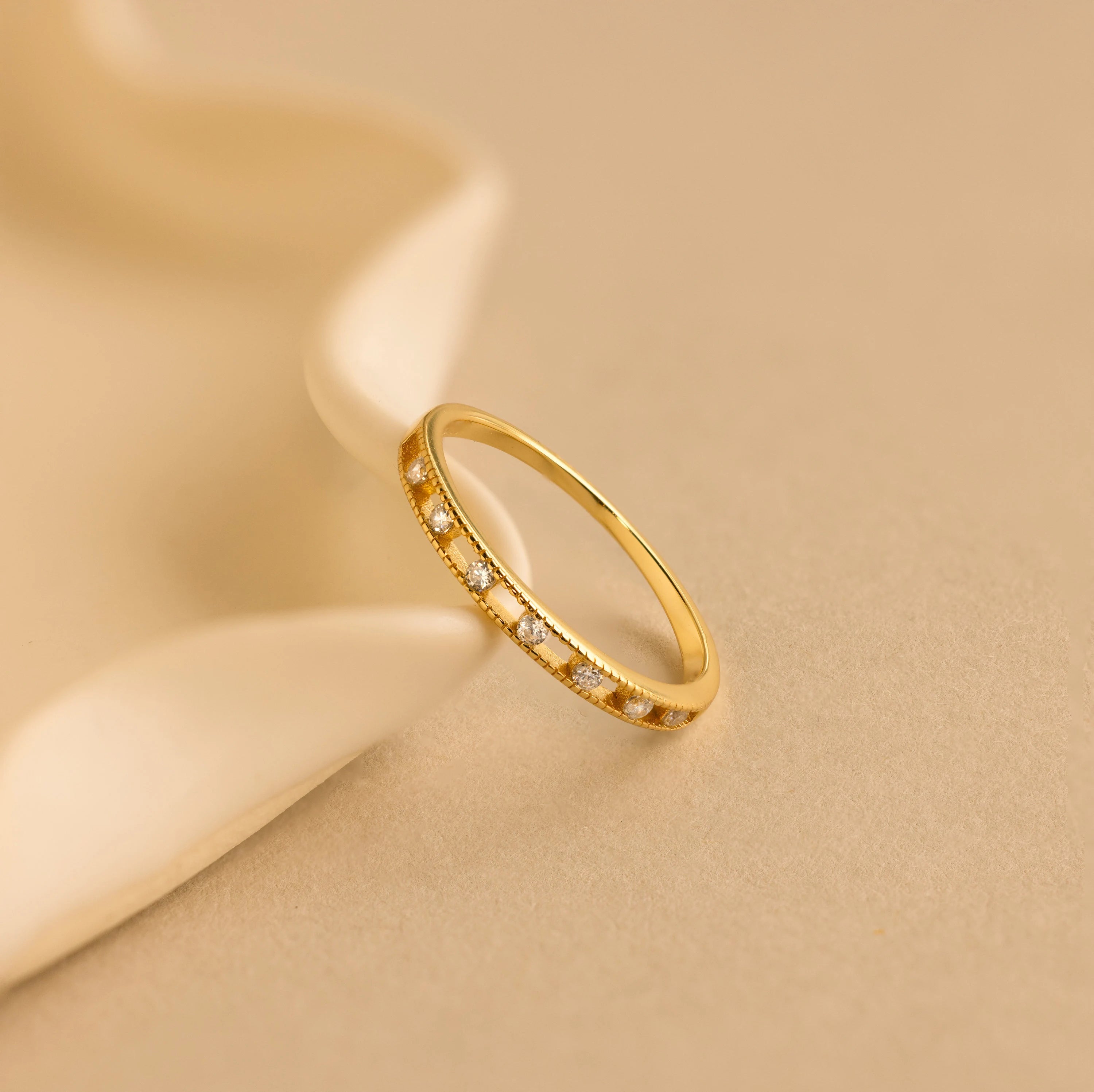 The Diamond Station Ring lies on a soft beige surface next to a white ceramic dish.