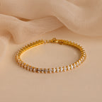 The Marquise Diamond Tennis Bracelet displayed flat on a beige fabric background, highlighting its sparkling marquise-cut stones and polished gold setting.