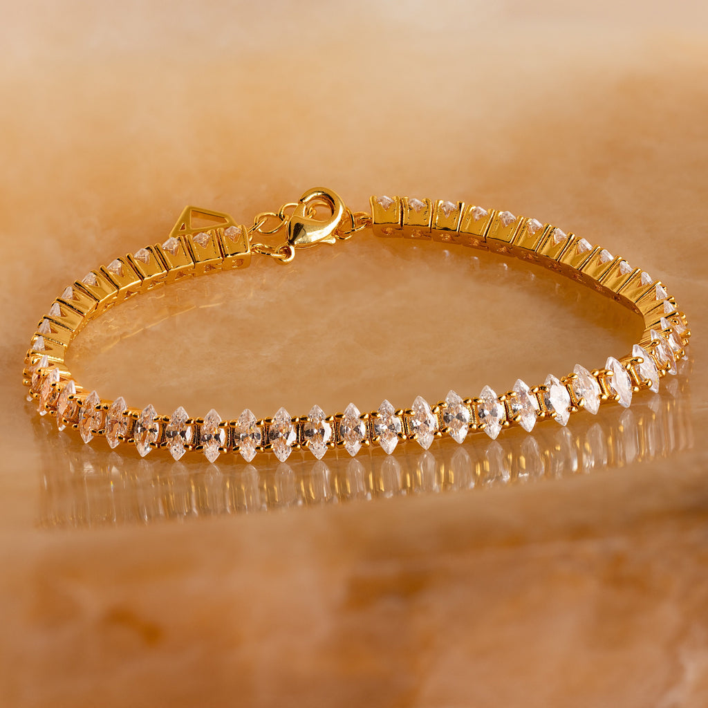 Close-up of the Marquise Diamond Tennis Bracelet featuring marquise-cut stones set in a gold band, displayed on a warm stone background.