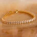Close-up of the Marquise Diamond Tennis Bracelet featuring marquise-cut stones set in a gold band, displayed on a warm stone background.