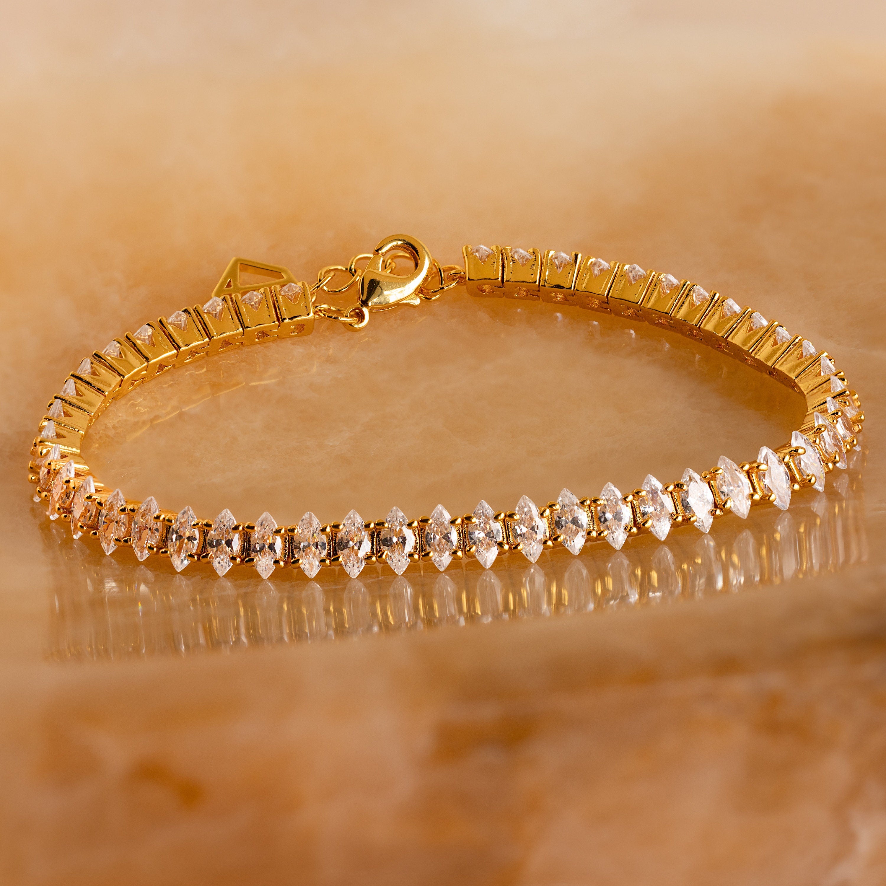 Close-up of the Marquise Diamond Tennis Bracelet featuring marquise-cut stones set in a gold band, displayed on a warm stone background.