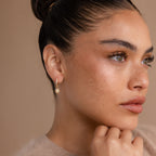 Woman with brown hair in a bun wearing Pave Opal Star Huggies, looking thoughtfully to the side.