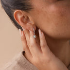 A woman touches her ear, showing off the Pave Opal Star Huggies—delicate hoop earrings adorned with a sparkling light blue opal star charm.