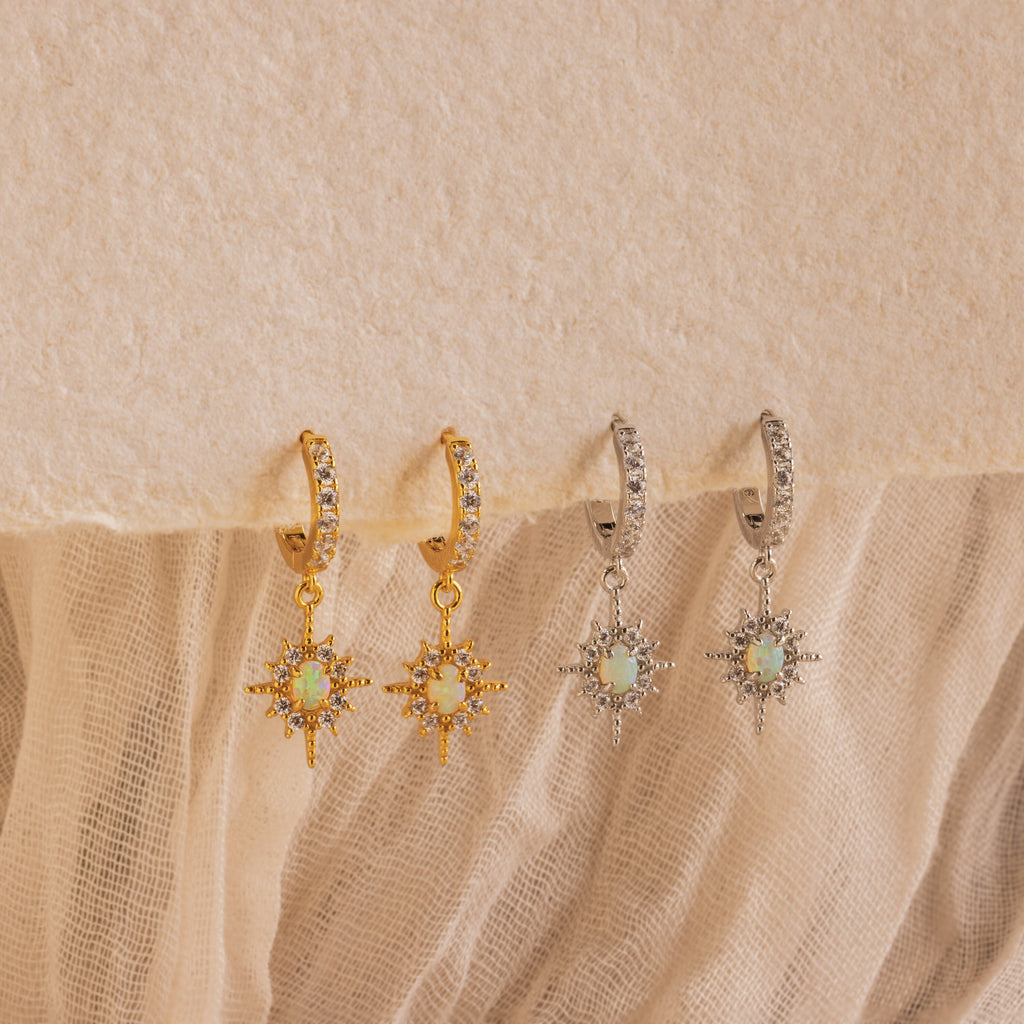 Pave Opal Star Huggies featuring sparkling starbursts with opal centers, showcased on a textured fabric background.