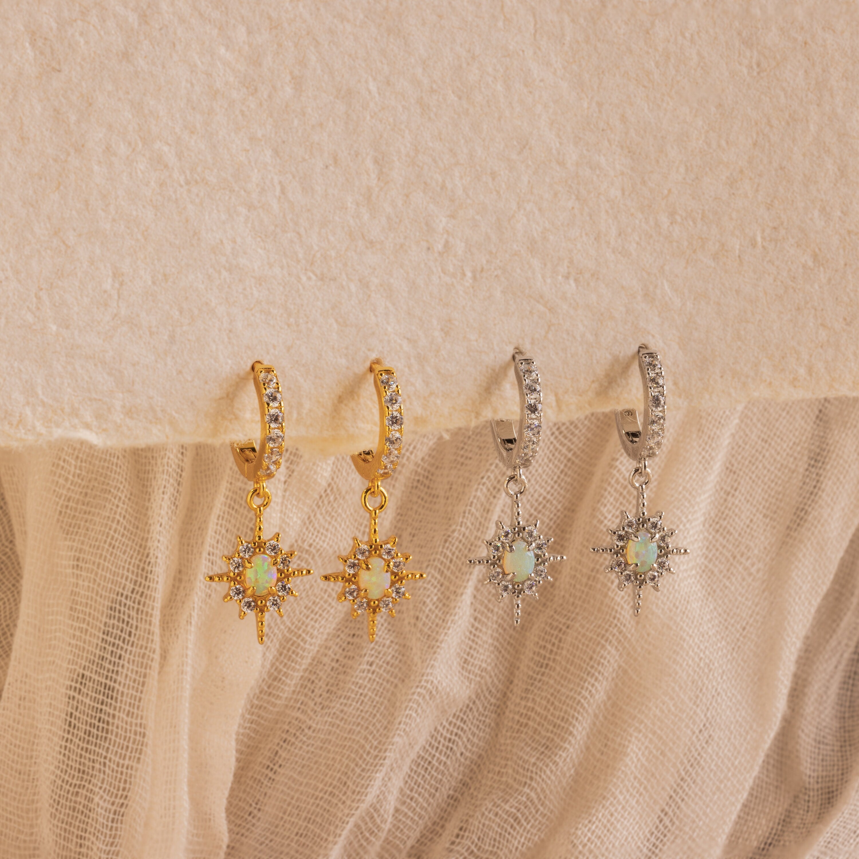 Pave Opal Star Huggies featuring sparkling starbursts with opal centers, showcased on a textured fabric background.