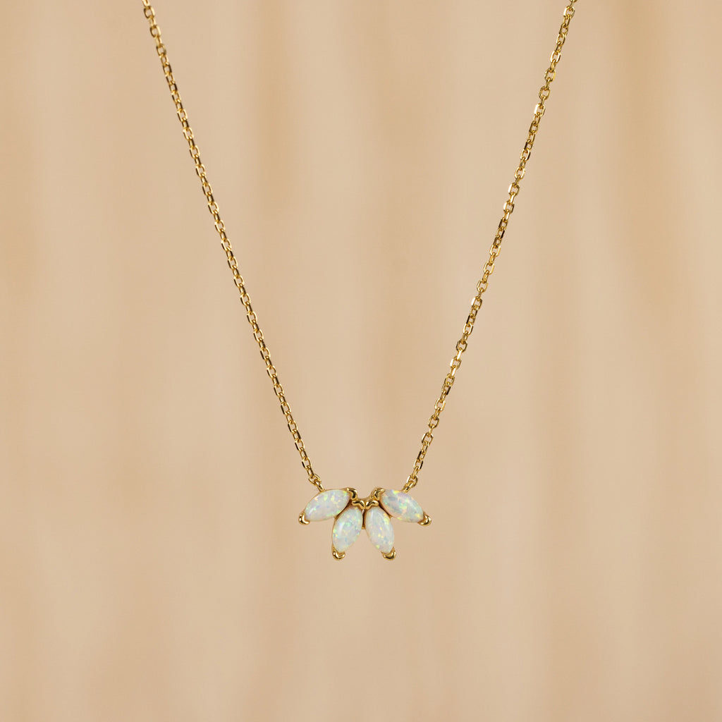 The White Opal Marquise Necklace features five marquise opal-like stones in a floral design, accented with gold and shown on a beige background.