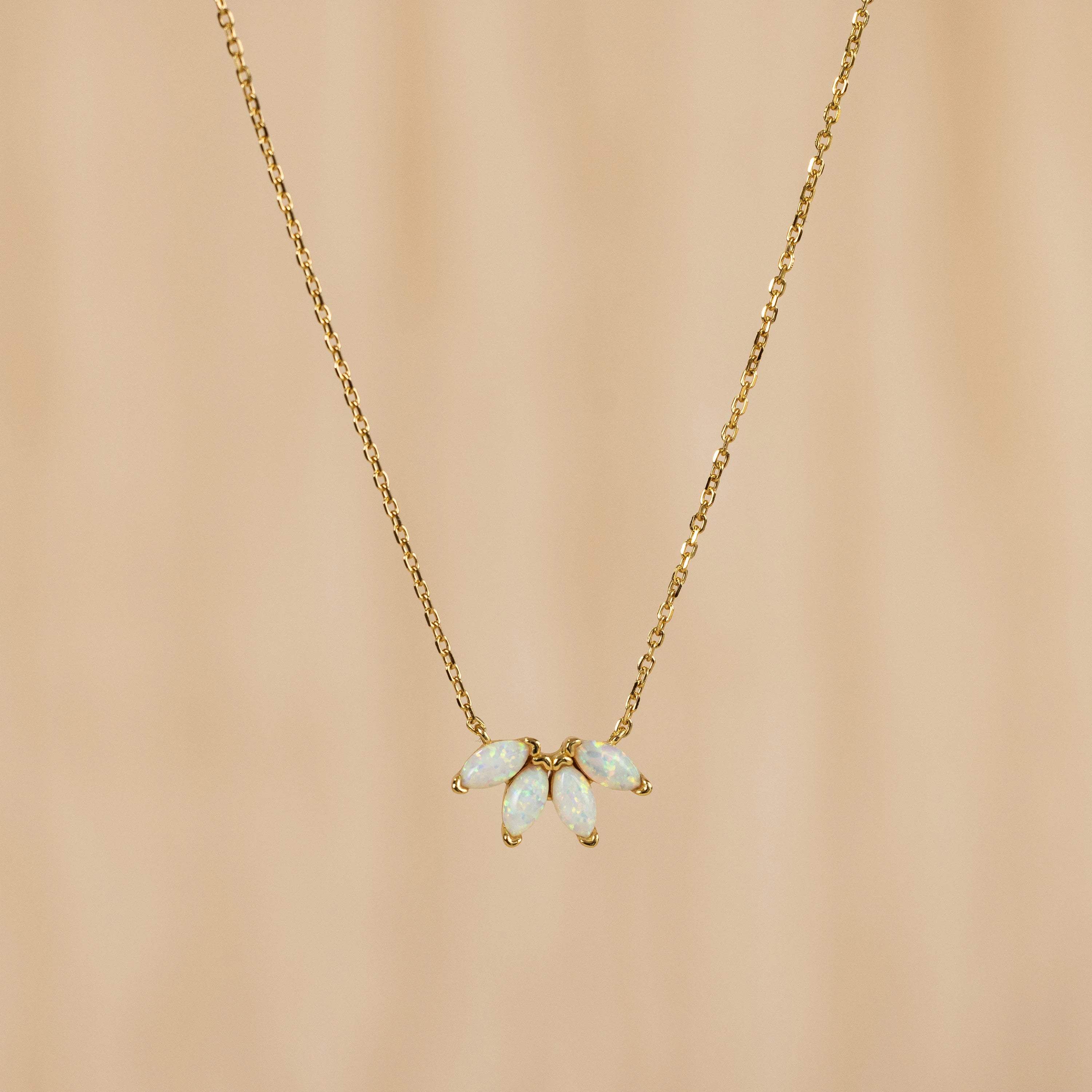The White Opal Marquise Necklace features five marquise opal-like stones in a floral design, accented with gold and shown on a beige background.