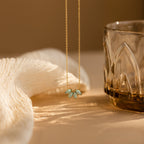 The Turquoise Opal Marquise Necklace rests beside a textured glass and soft white fabric on a beige surface.