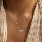 A woman wearing a cream textured top showcases the Turquoise Opal Marquise Necklace, a gold necklace featuring five marquise turquoise stones.