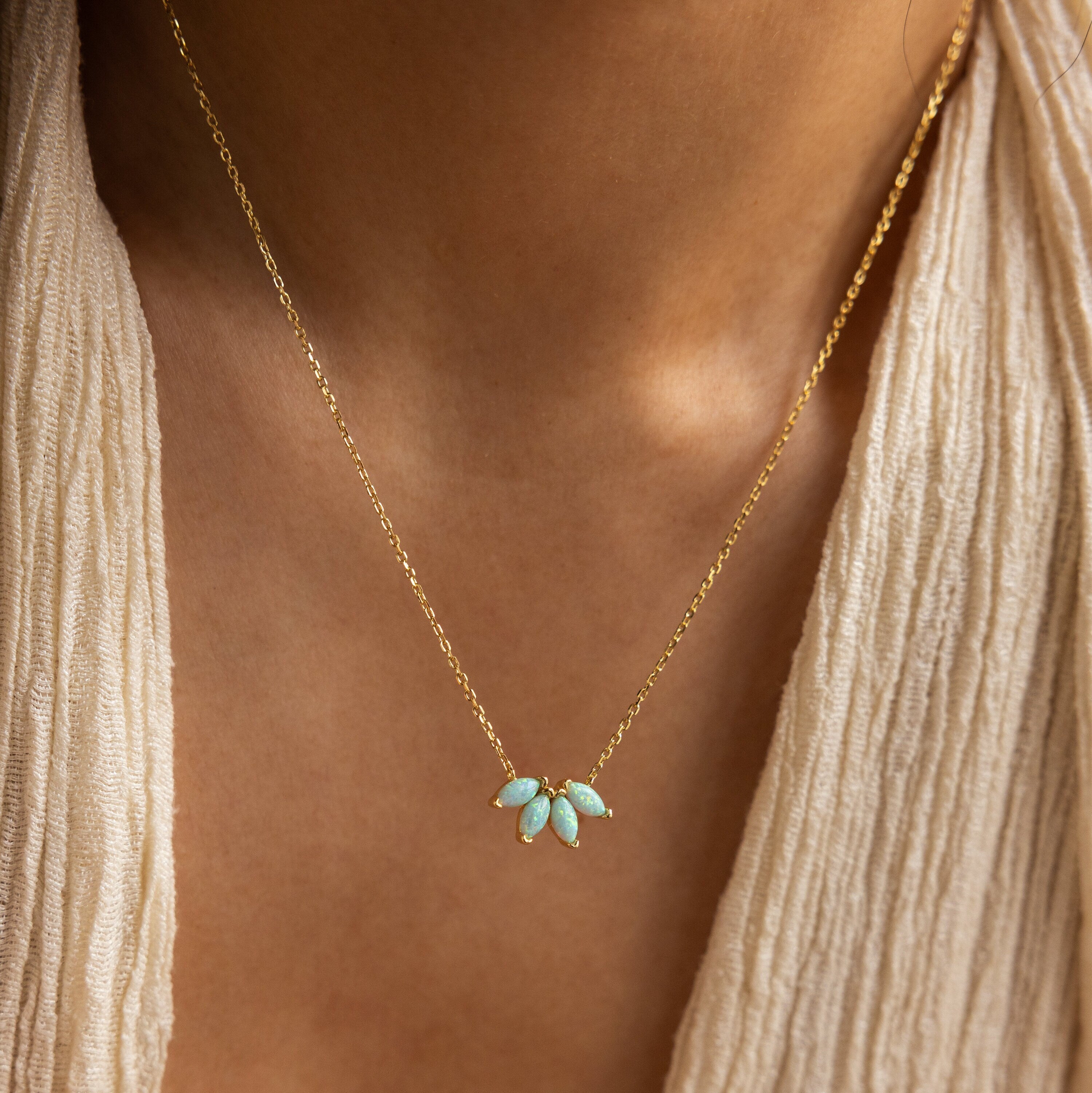 A woman wearing a cream textured top showcases the Turquoise Opal Marquise Necklace, a gold necklace featuring five marquise turquoise stones.