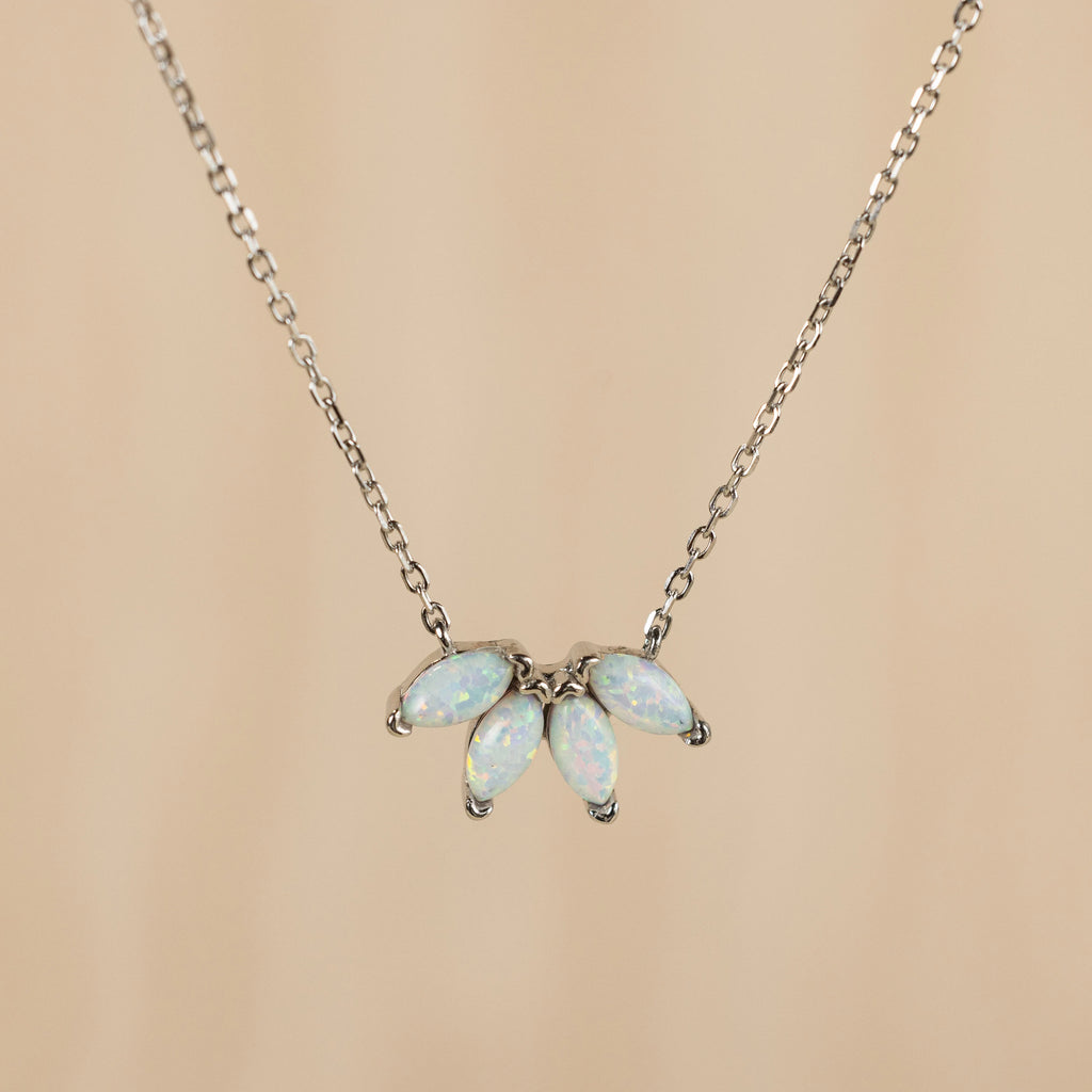 The White Opal Marquise Necklace features five marquise opal stones in a fan shape on a silver chain, adding elegance to your gemstone collection. Shown against a beige background.